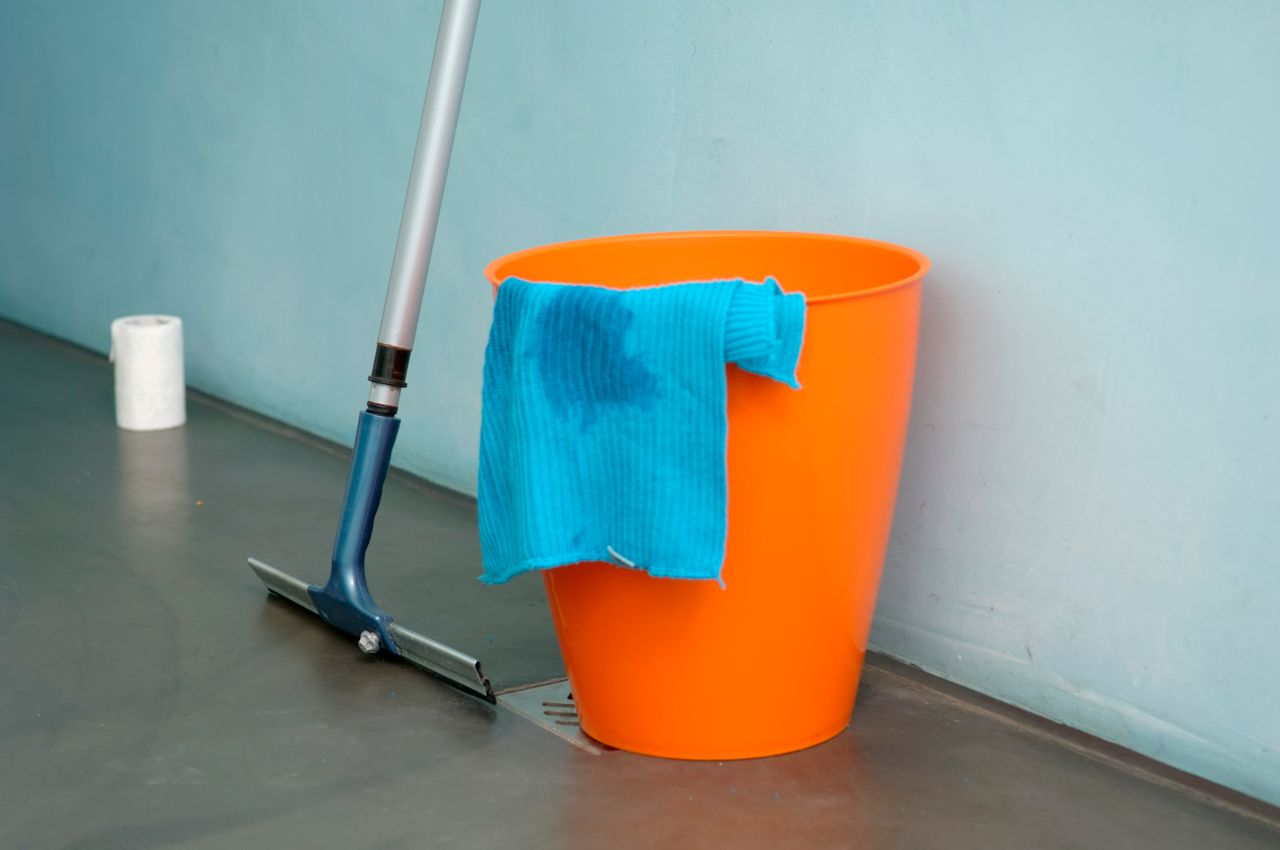 About Close-up of cleaning supplies including orange bucket, mop, and blue rag indoors.