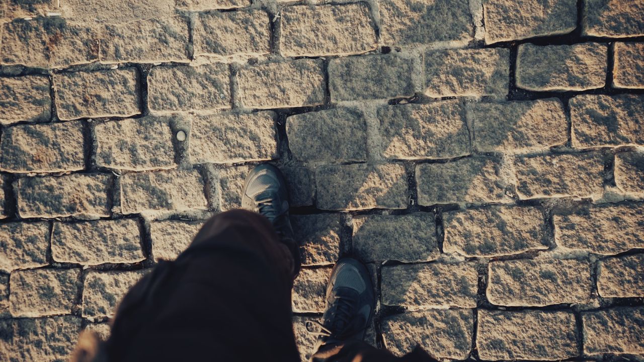 Top view of person walking on a sunlit cobblestone street, casting shadows.